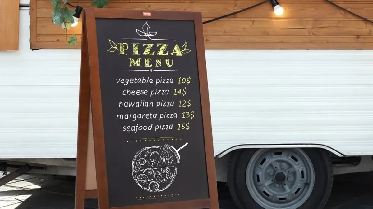 black A-frame chalkboard menu board with pizza menu in front of a food truck
